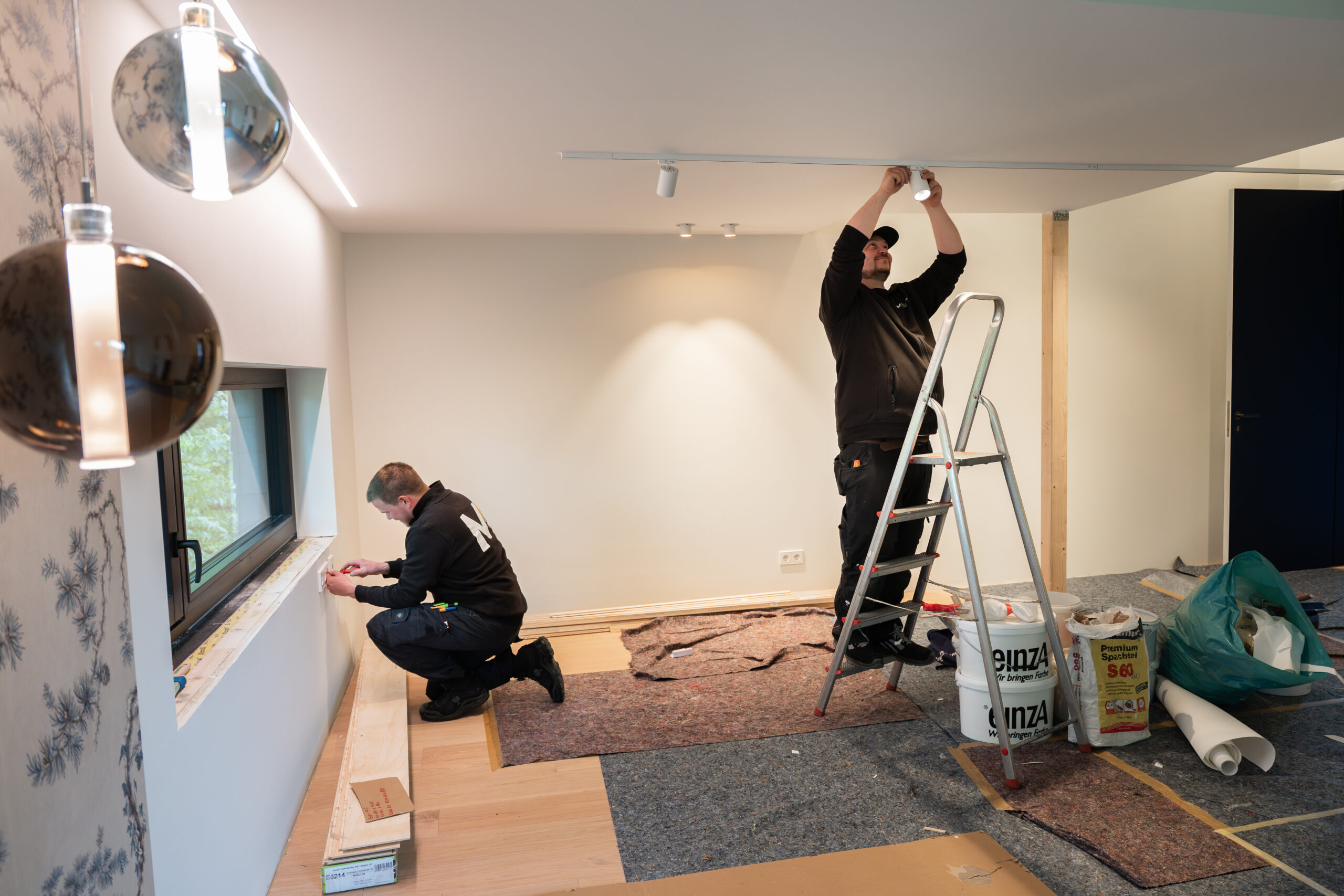 Zwei Elektriker von Elektro Mersmann installieren Schienensystem und Beleuchtung im Wohnraum – Lichtinstallation in Harsewinkel
