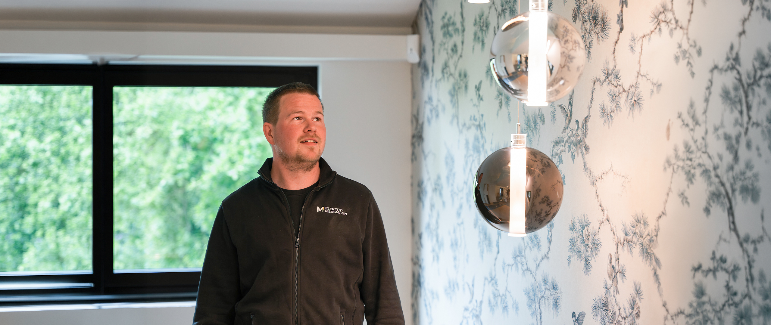 Aaron Mersmann, Inhaber von Elektro Mersmann aus Harsewinkel, begutachtet eine hochwertige Pendelleuchten-Installation im modernen Wohnraum
